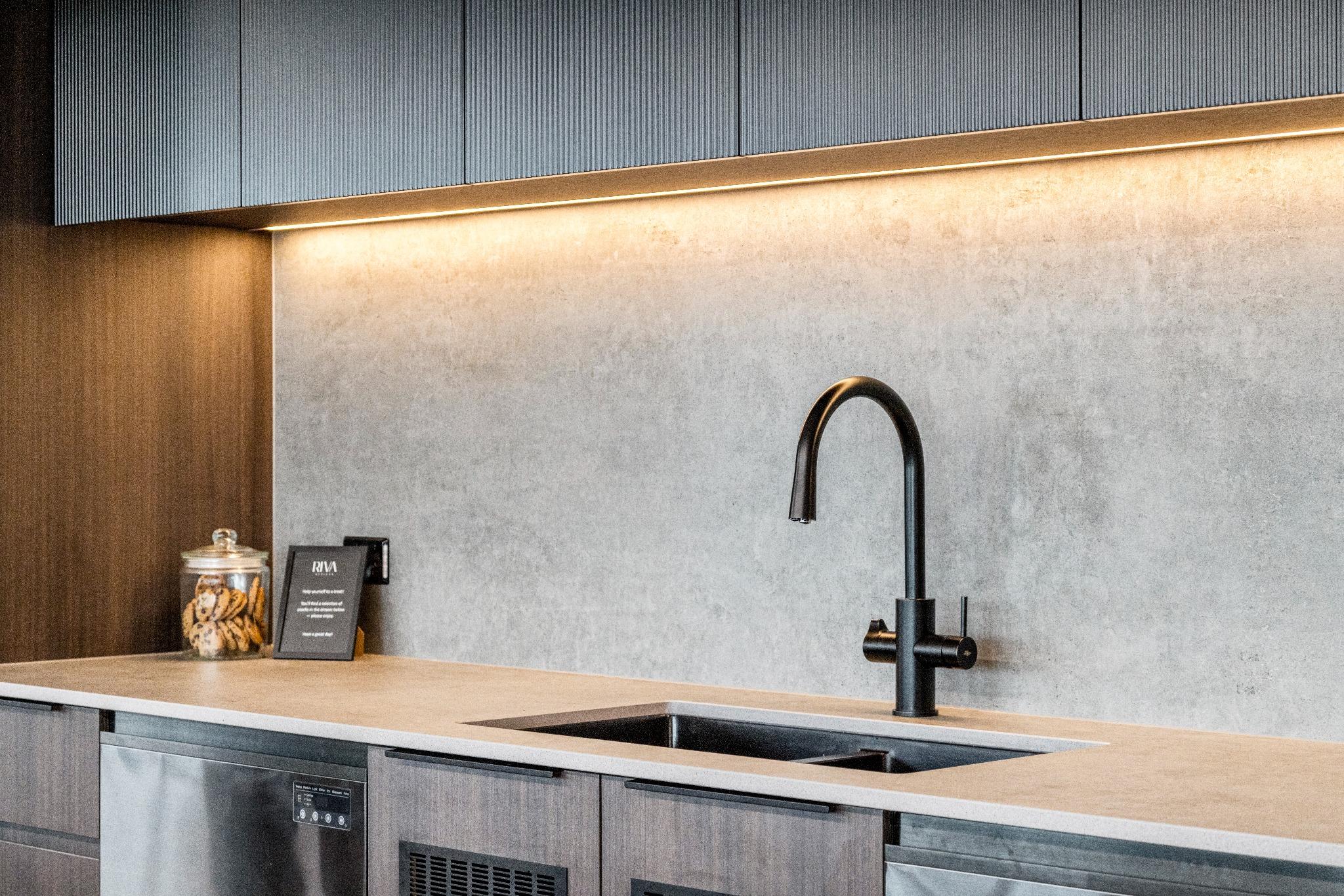Under-bench lighting and black tapware in a compact kitchenette designed for modern office environments.