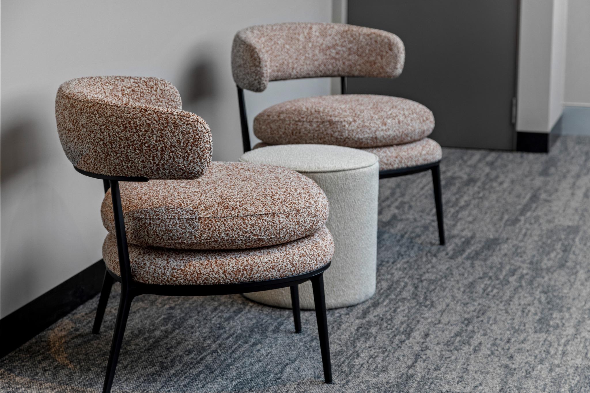 Breakout lounge seating at Riva Robina featuring sculptural low-back armchairs in a soft neutral upholstery, positioned around a pale coffee table with natural light filtering in from adjacent offices.