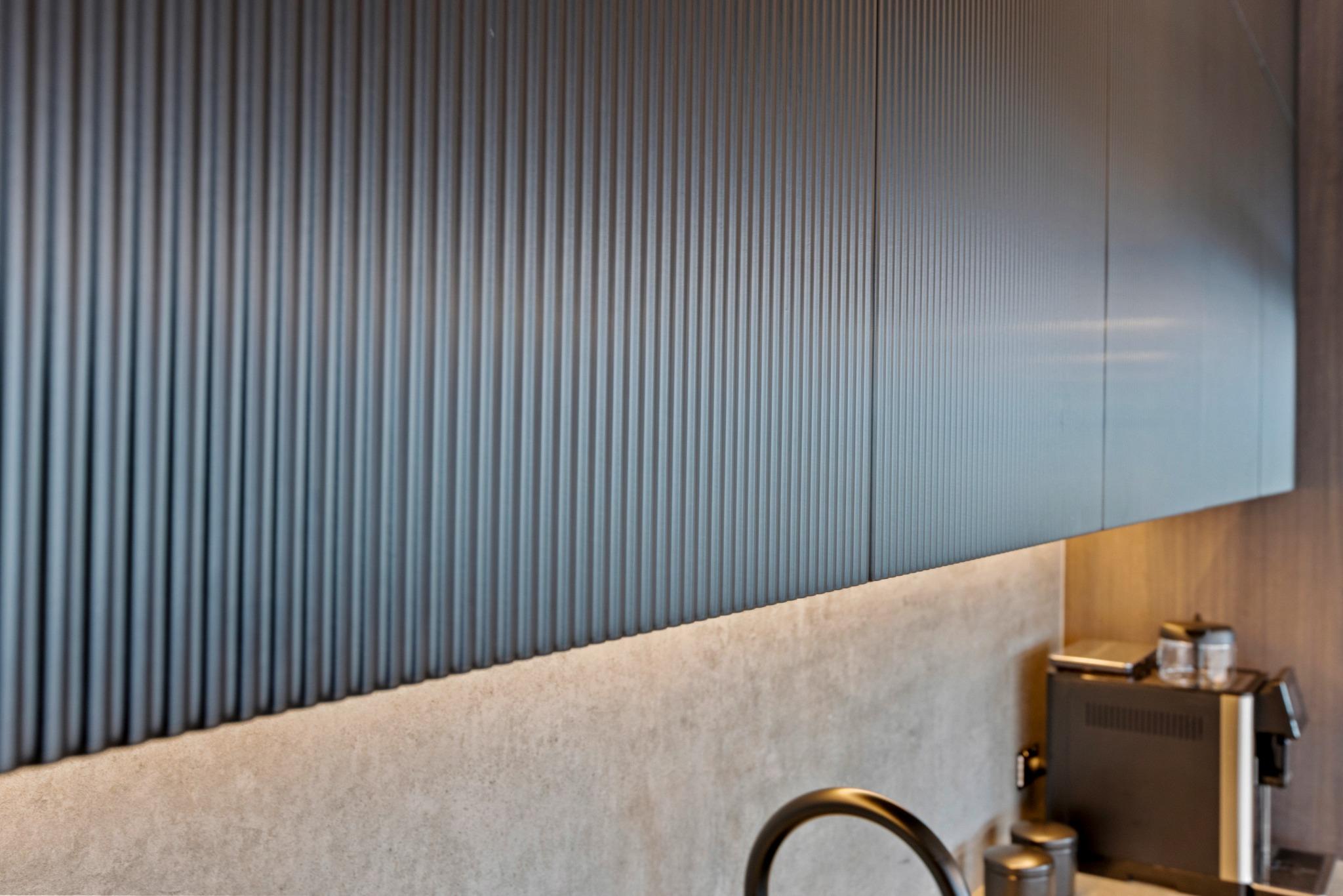 Overhead kitchen joinery at Riva Robina finished in Polytec, featuring vertical grain panels, push-to-open doors, and concealed LED strip lighting for a clean, minimalist finish.