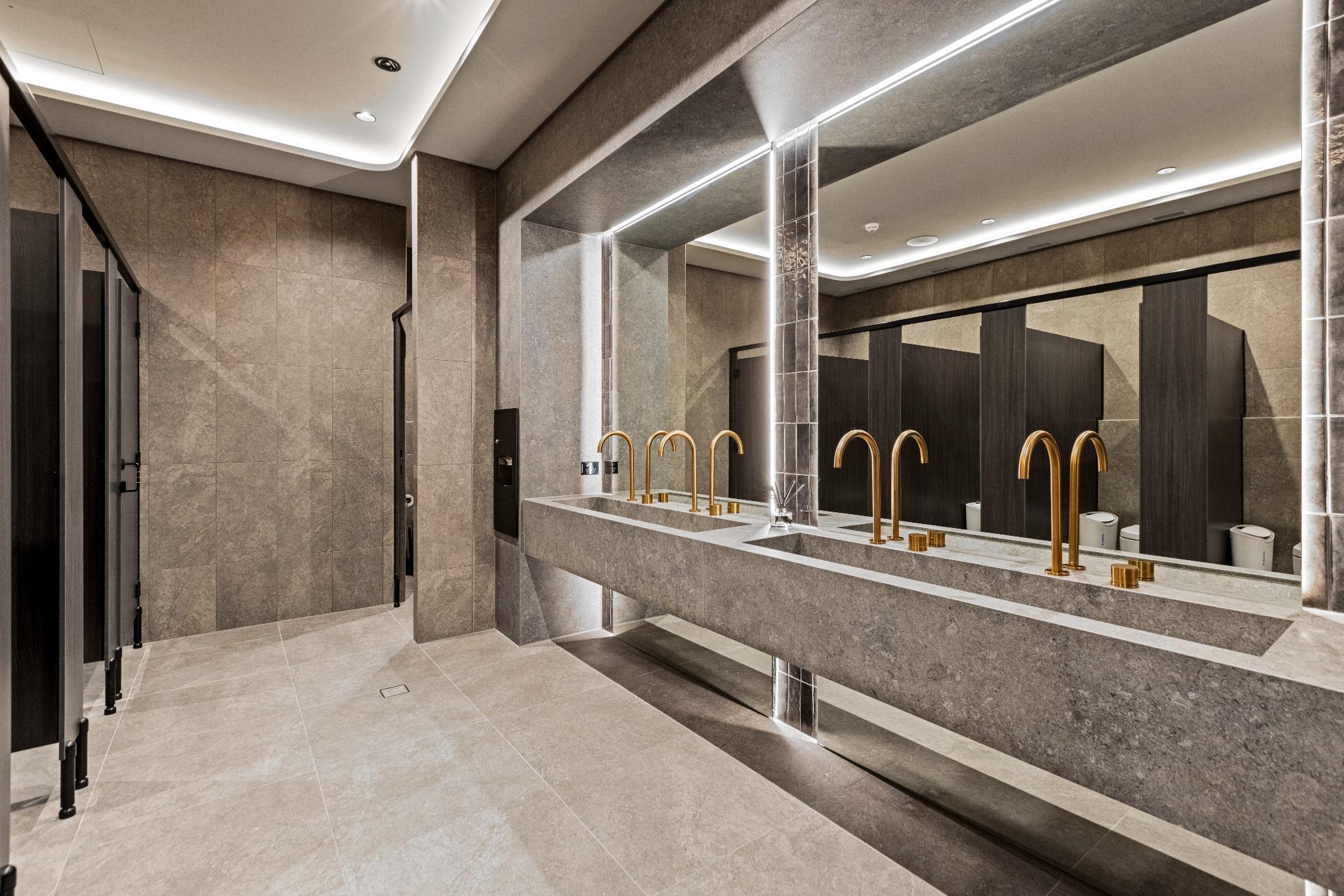 Floating stone vanity with integrated dual sinks and brushed brass tapware in a high-end commercial bathroom fitout.