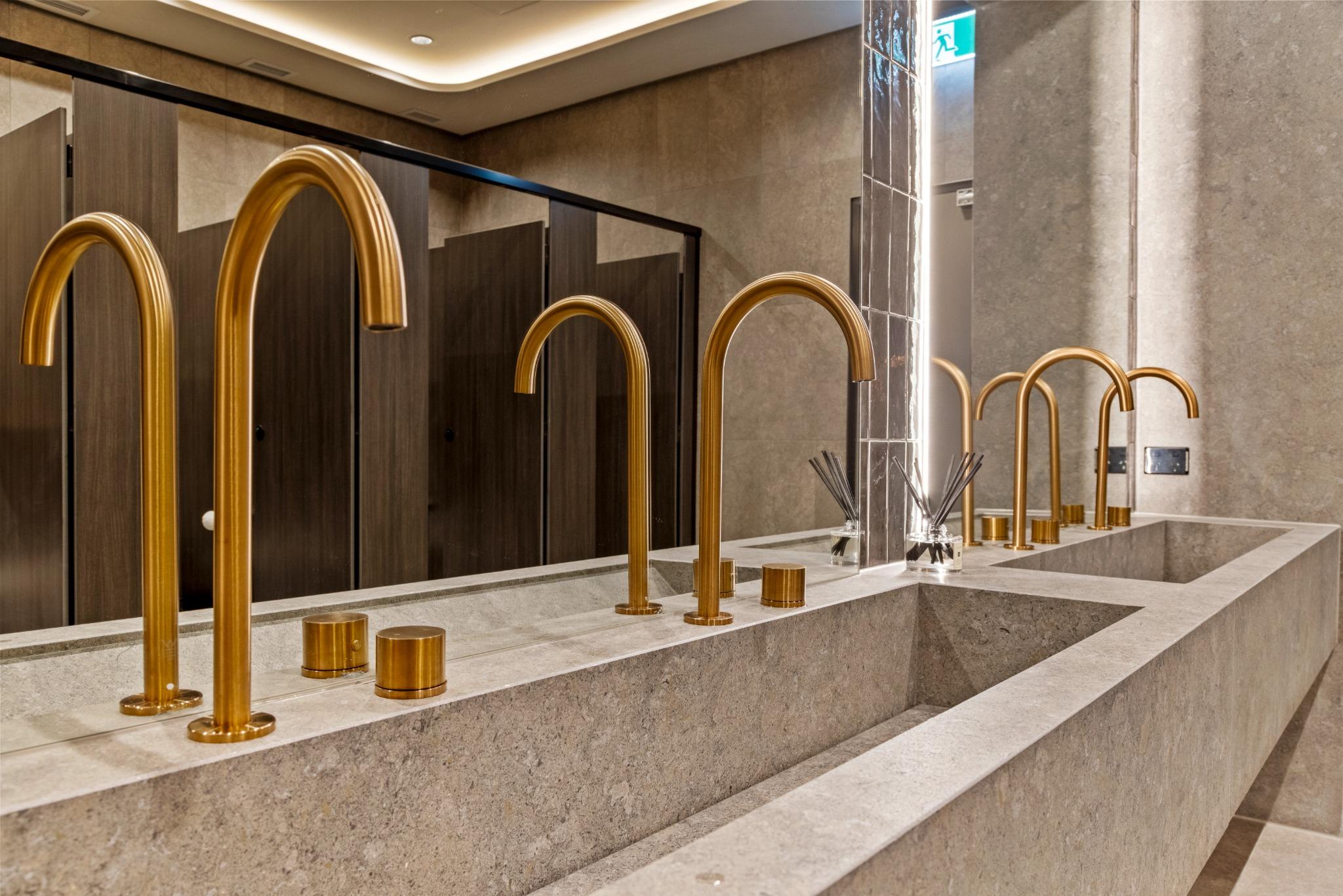Brushed gold tapware and double stone vanity bench in a professionally detailed commercial washroom.