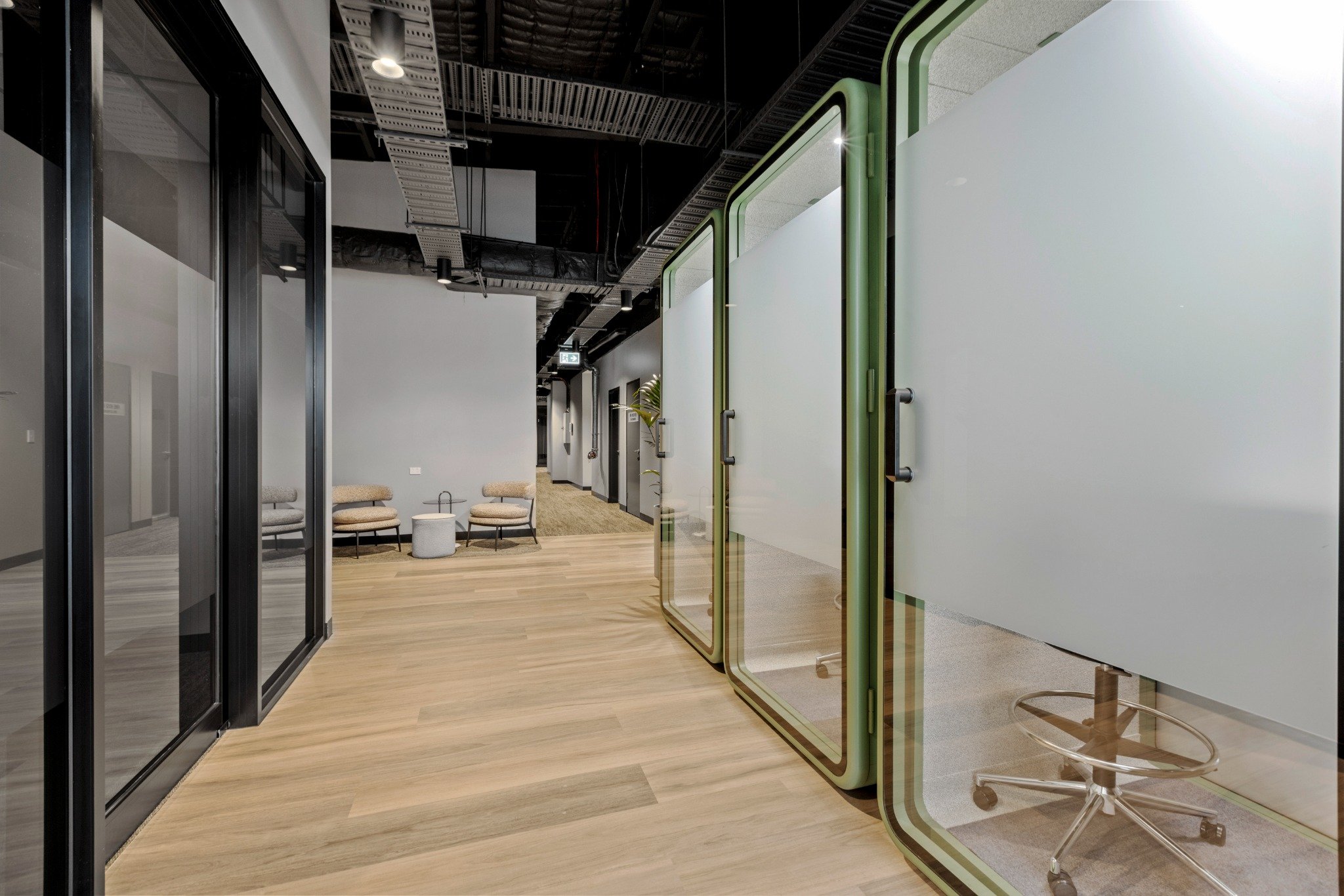 Frosted glass privacy pods and light oak flooring in a modern, professional workspace hallway.