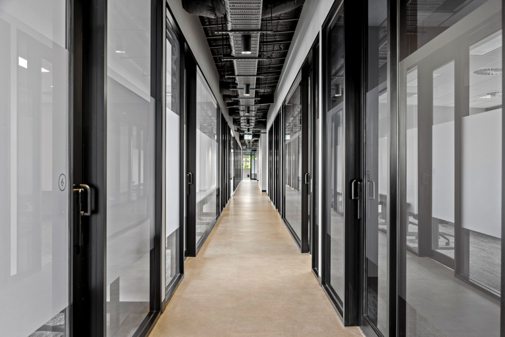 Glass corridor with symmetrical glazing and visible ceiling services for an industrial office fitout aesthetic.