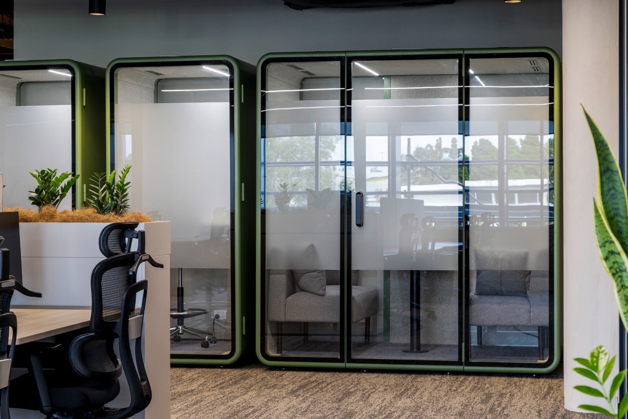 Private office pods with green frames and acoustic glazing in a commercial co-working space interior.