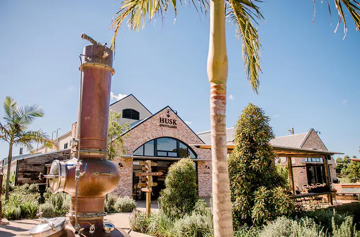 Husk Distilleries building exterior with copper distillation equipment, surrounded by lush greenery and palm trees, showcasing a hospitality venue in North Tumbulgum, NSW.