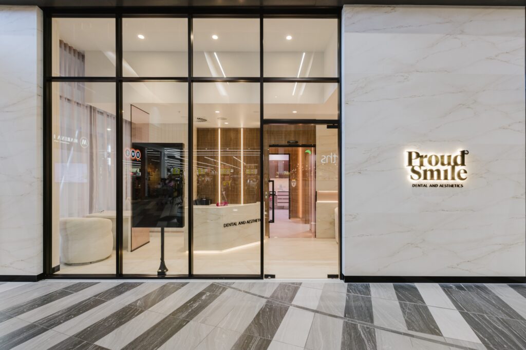 Proud Smile dental clinic entrance showcasing modern design with marble facade, illuminated signage, and inviting reception area.