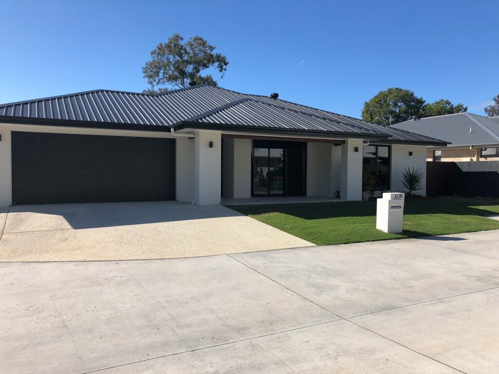 Modern residential home in Queensland, featuring a sleek design with a dark roof, large windows, and a manicured lawn, showcasing the work of Leithal Designs.