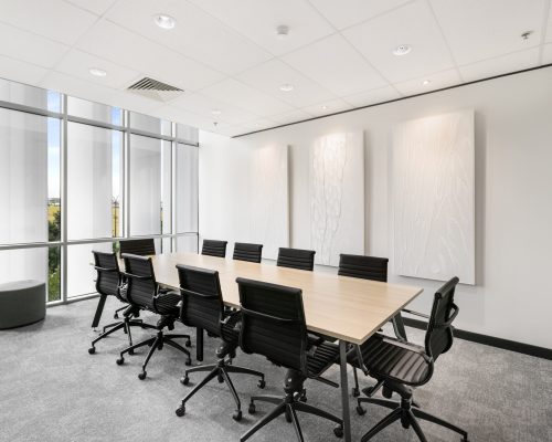 Modern conference room featuring a long wooden table surrounded by black ergonomic chairs, illuminated by natural light from large windows, with textured white wall art enhancing the sophisticated design, reflecting Leithal Designs' focus on premium commercial environments.