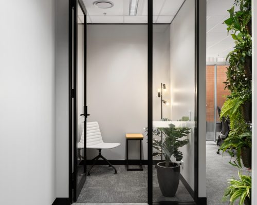Modern office space featuring a glass-walled meeting room with a white chair, small wooden table, and greenery, illustrating Leithal Designs' focus on design-led commercial environments and high-performing workplaces.