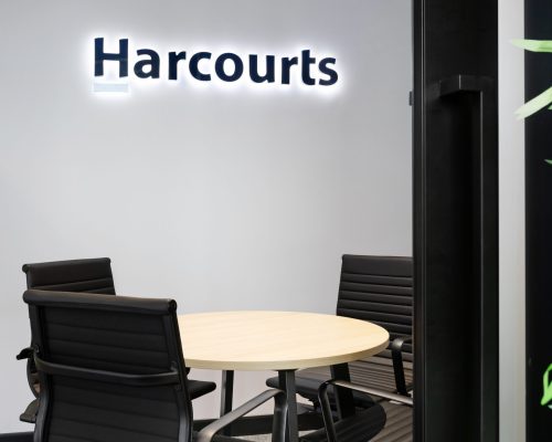 Harcourts branded meeting room featuring a round table and black ergonomic chairs, designed for collaborative discussions in a professional commercial fit-out context.