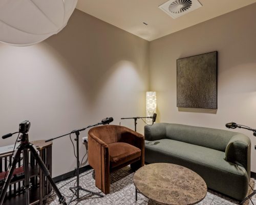 Commercial recording studio setup featuring a green sofa, brown armchair, round marble table, and microphones, emphasizing design-led functionality and premium aesthetics for creative environments.