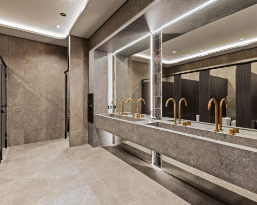 Luxury commercial restroom design featuring elegant gold faucets, spacious marble sinks, and modern lighting, reflecting Leithal Designs' focus on premium materials and sophisticated aesthetics for high-end fit-outs.