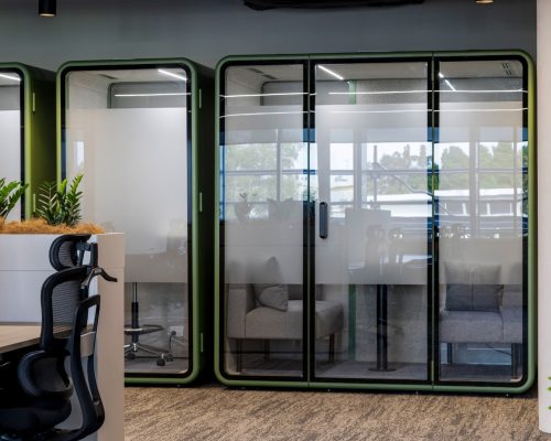 Modern glass meeting rooms with green frames in a commercial office space, showcasing strategic design and functionality for high-performing workplaces.