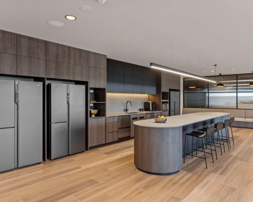 Modern commercial kitchen with sleek cabinetry, stainless steel appliances, and a large circular island, emphasizing premium design and functionality for high-performing workplaces.